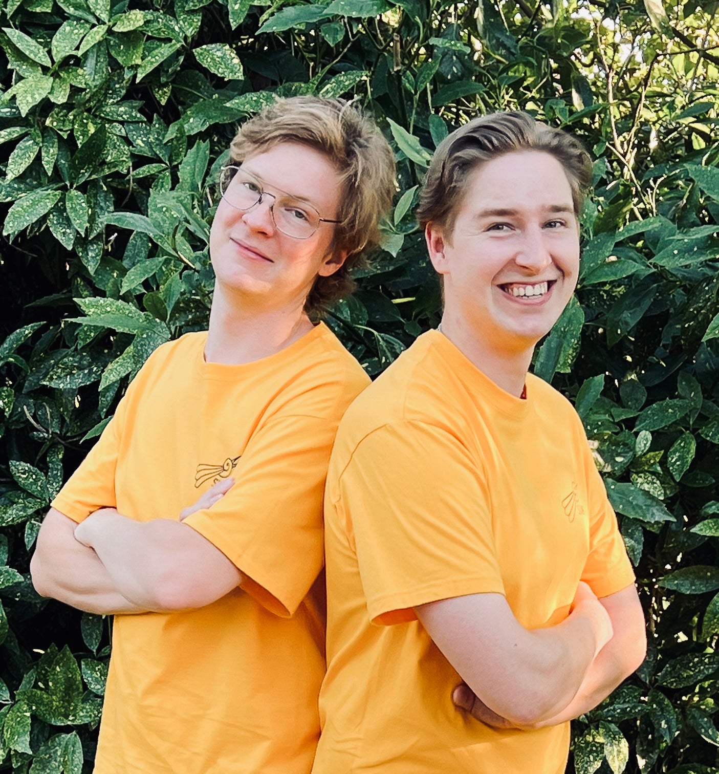 Two people wearing yellow shirts standing in front of green foliage